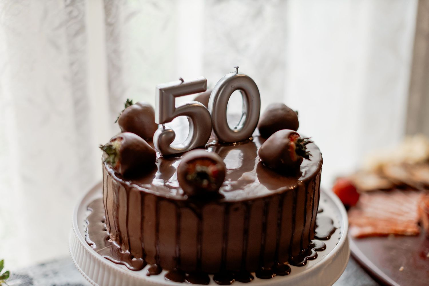 Chocolate drip birthday cake with chocolate-covered strawberries and number 50 candles for a 50th birthday celebration.