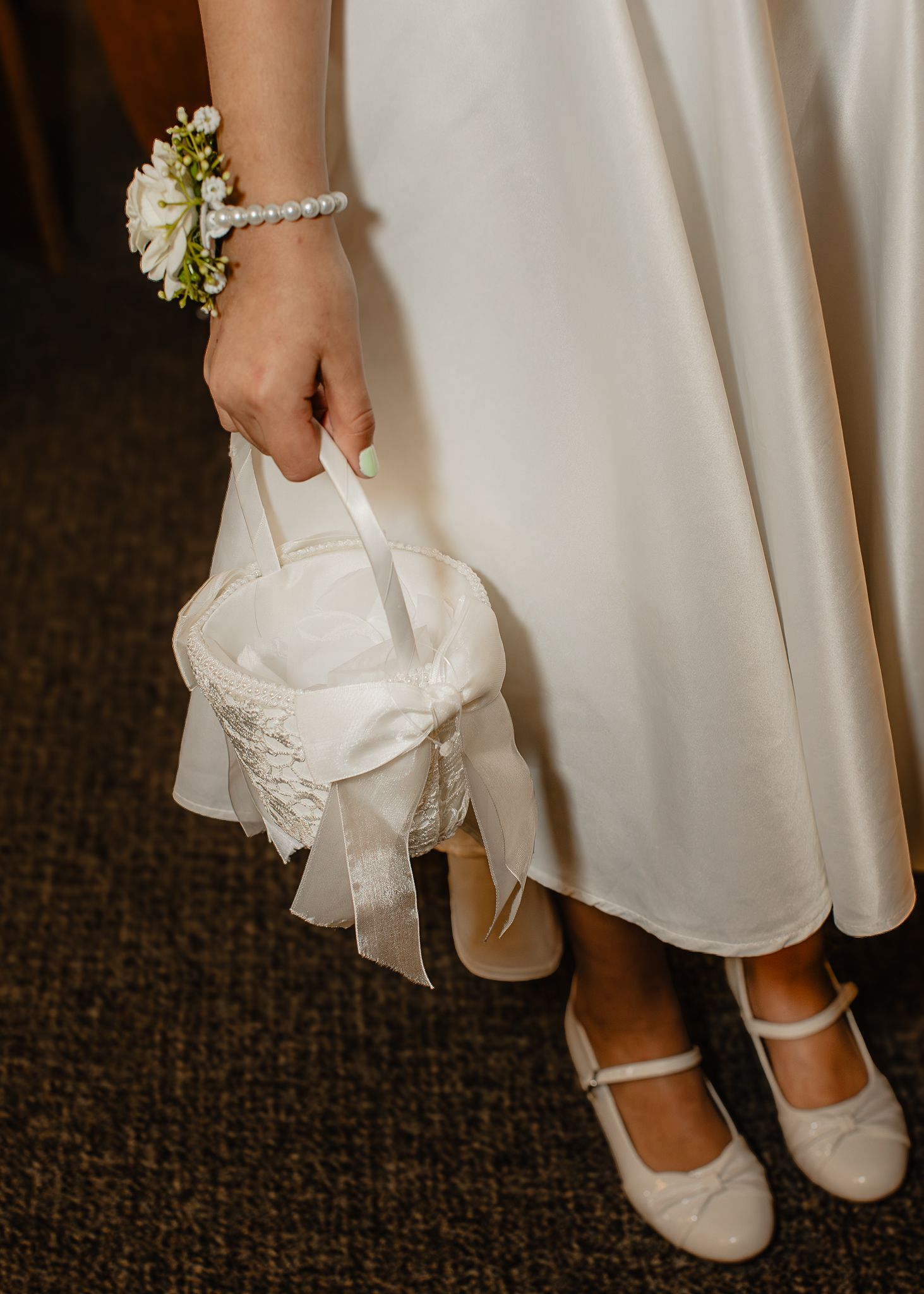 Bride holding a white flower girl basket with pearl bracelet and white Mary Jane shoes.