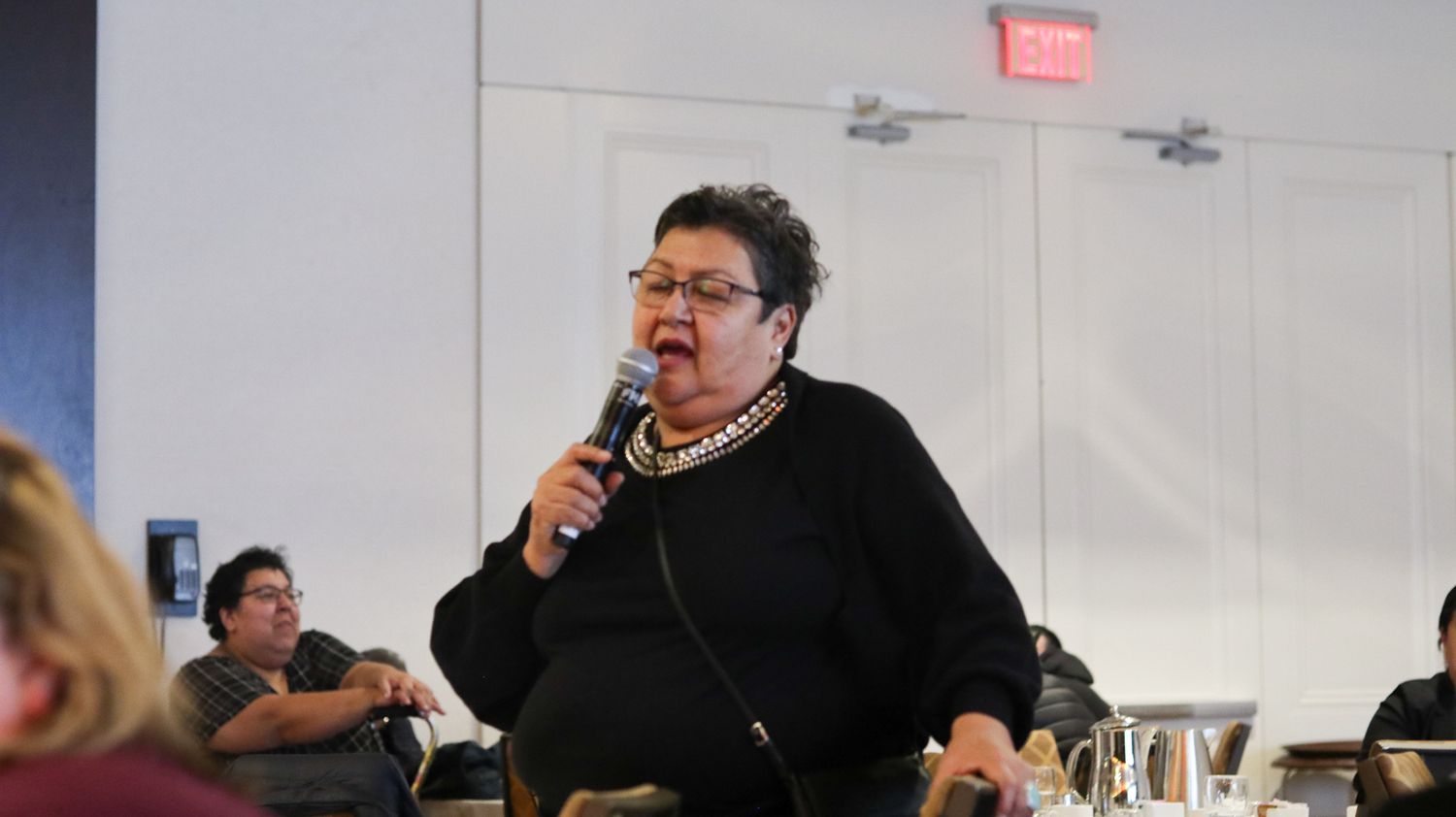 Indigenous woman speaking into a microphone at a conference or community meeting event.