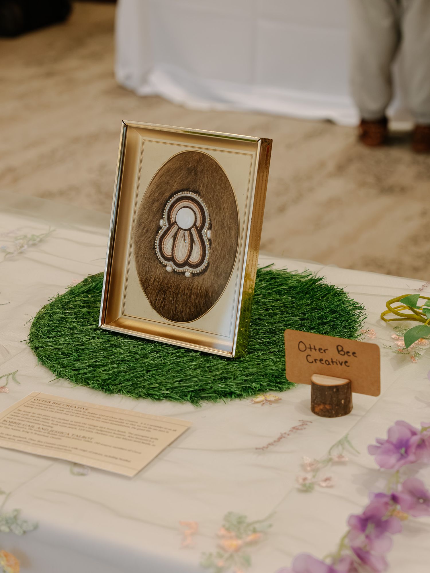Framed beaded artwork on fur backing displayed at Otter Bee Creative craft fair booth.