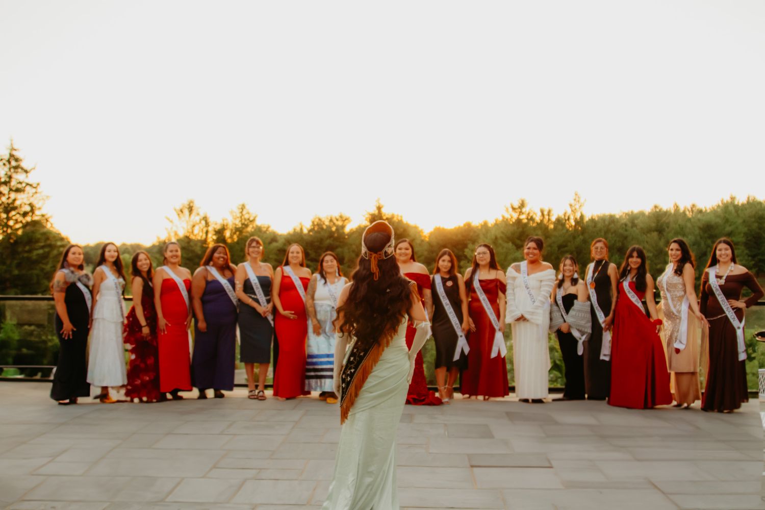 Formal group photo lineup outdoors with people wearing red and neutral colored attire.