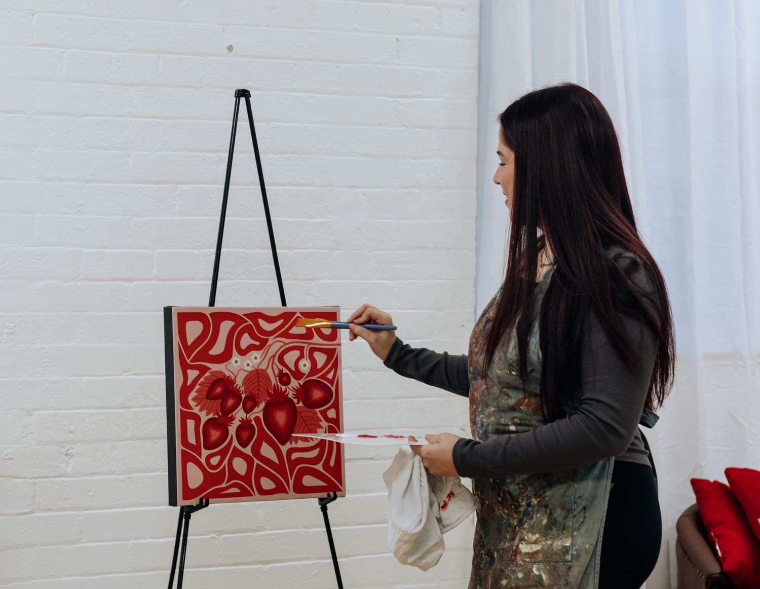 Artist working on red abstract artwork displayed on black easel.