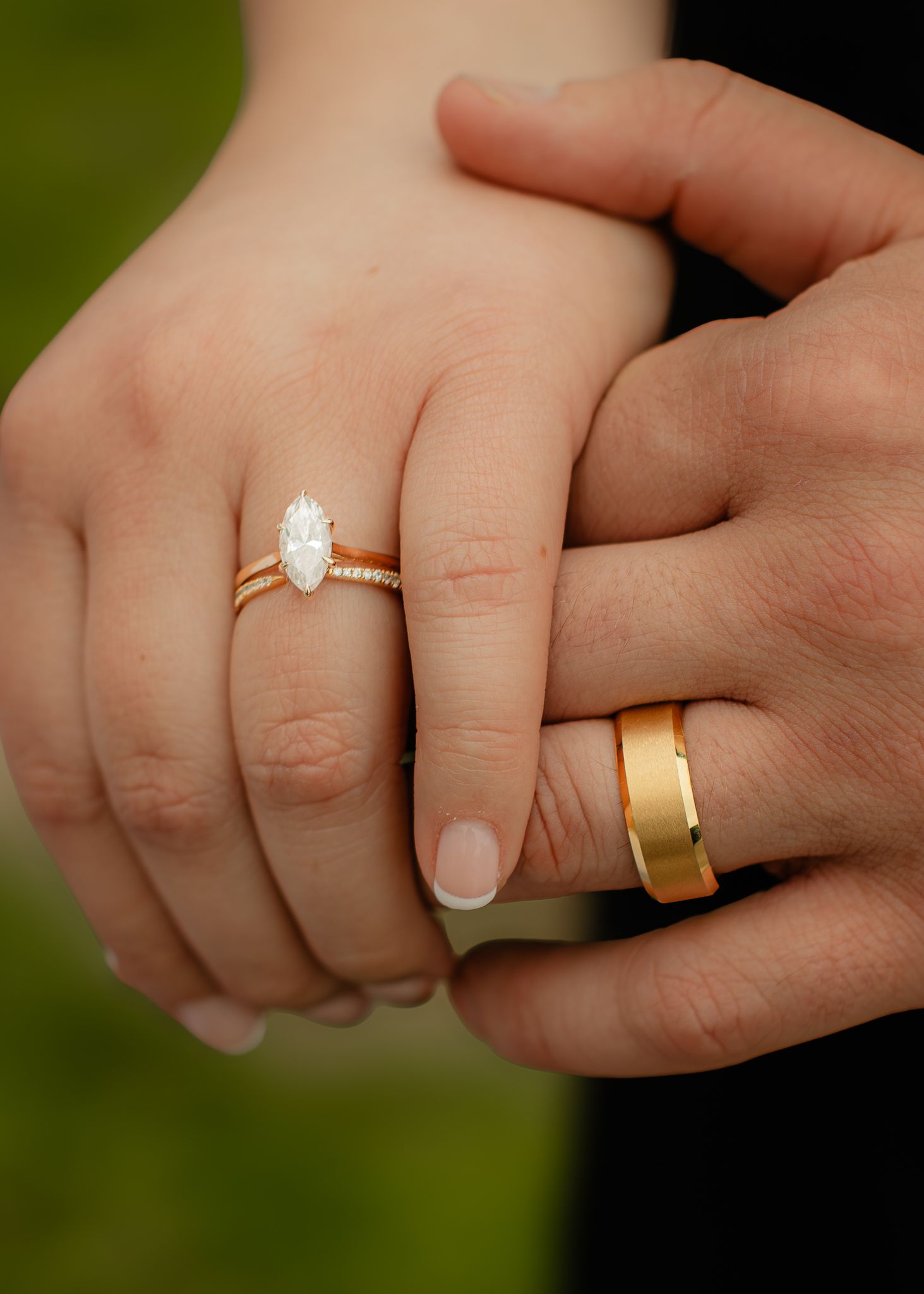 Close-up of bride's marquise diamond engagement ring and groom's gold wedding band as they hold hands.