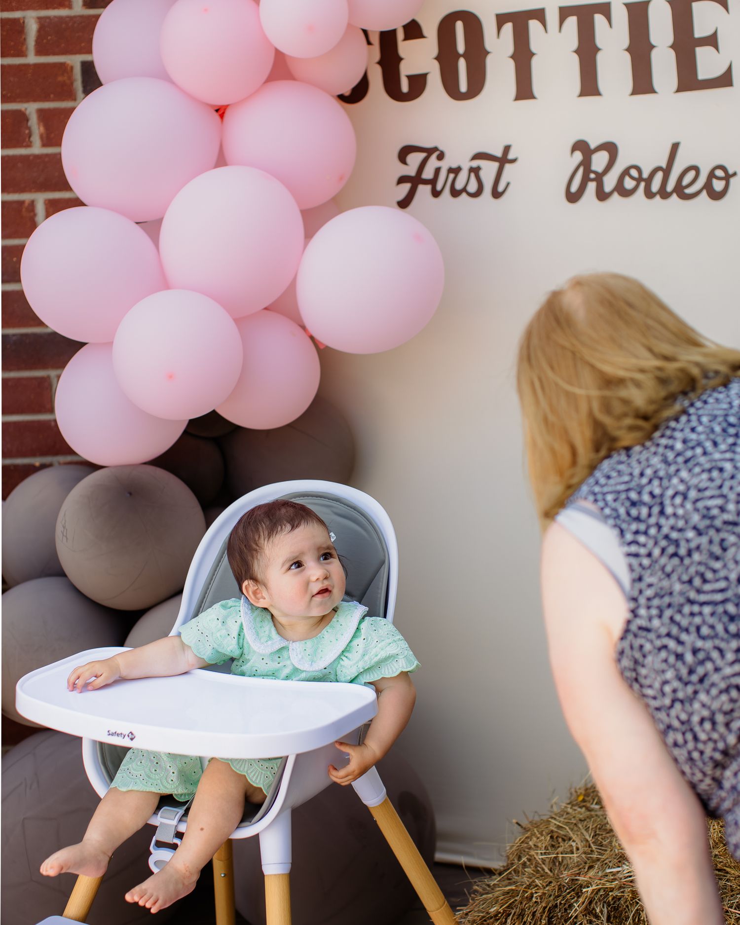 Baby girl in high chair at Scottie's First Rodeo birthday party with pink balloon decorations.