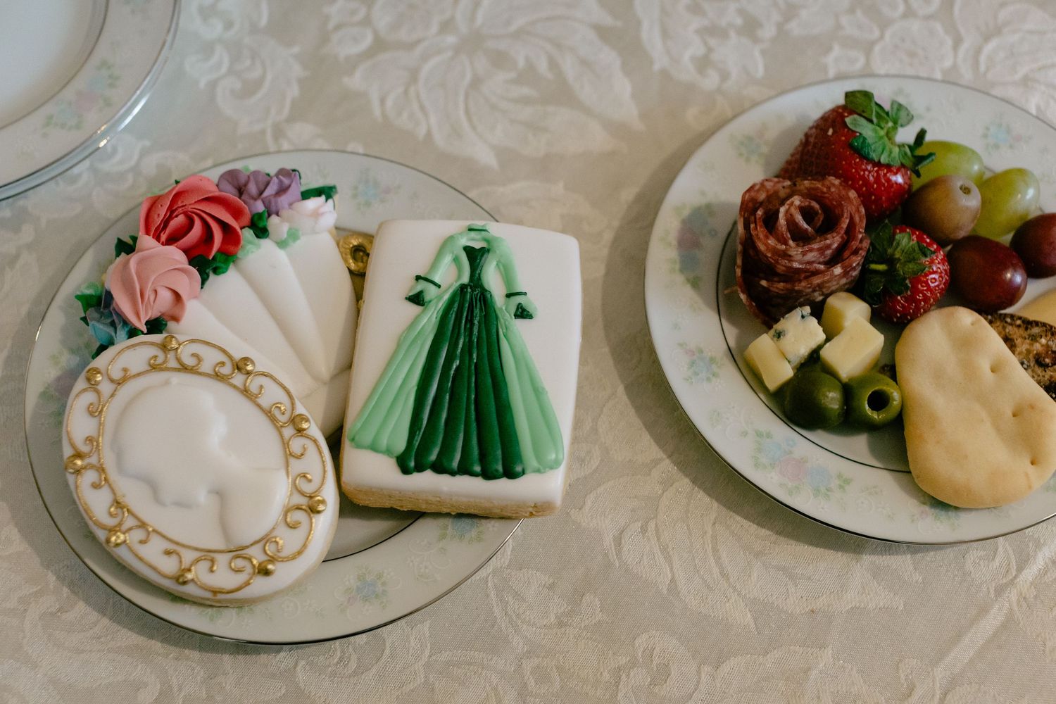 Decorative sugar cookies featuring a green gown and floral design displayed beside a charcuterie plate.