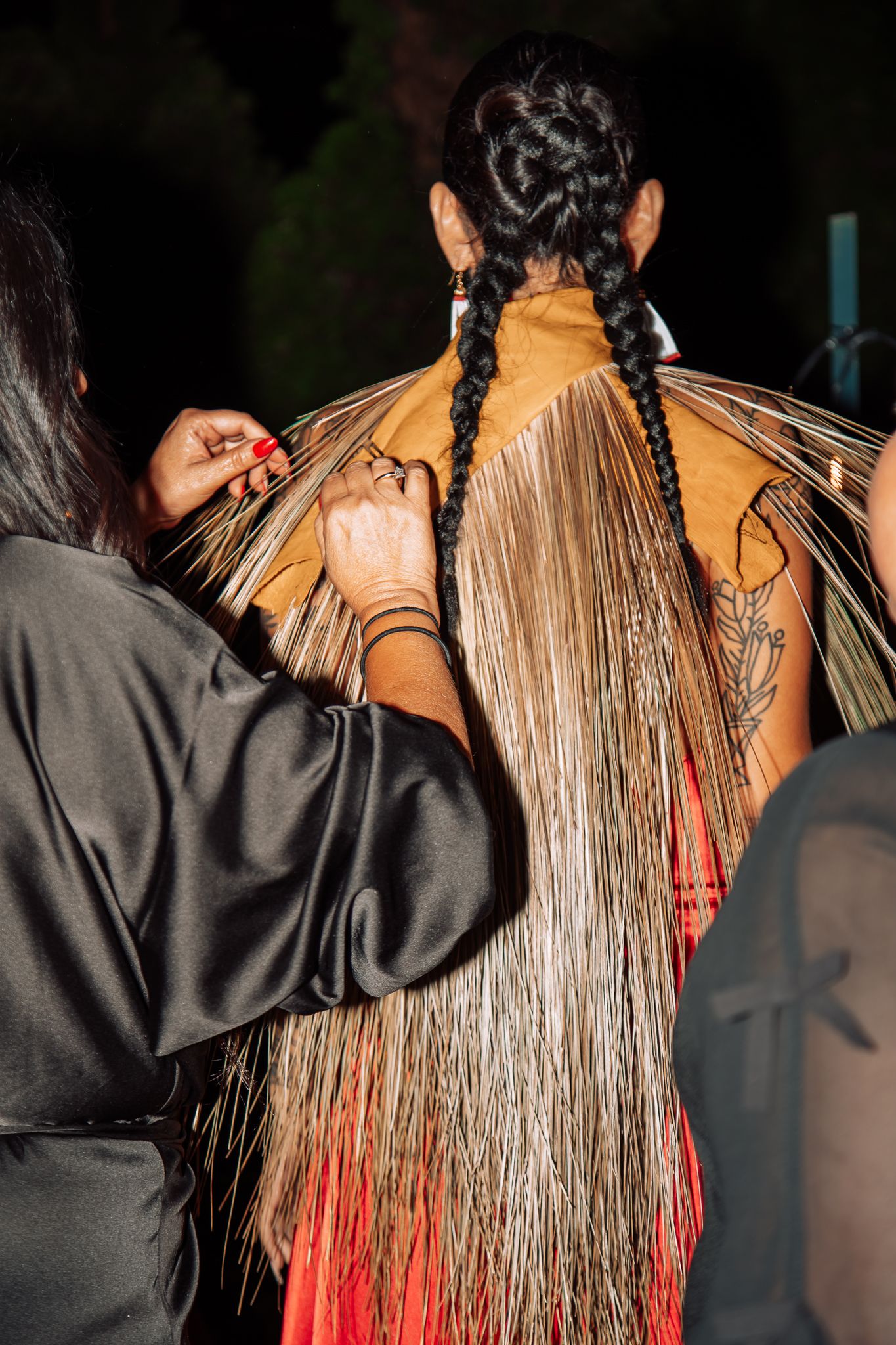 Person adjusting intricate fringe detail on tan leather garment with braided hair backstage.