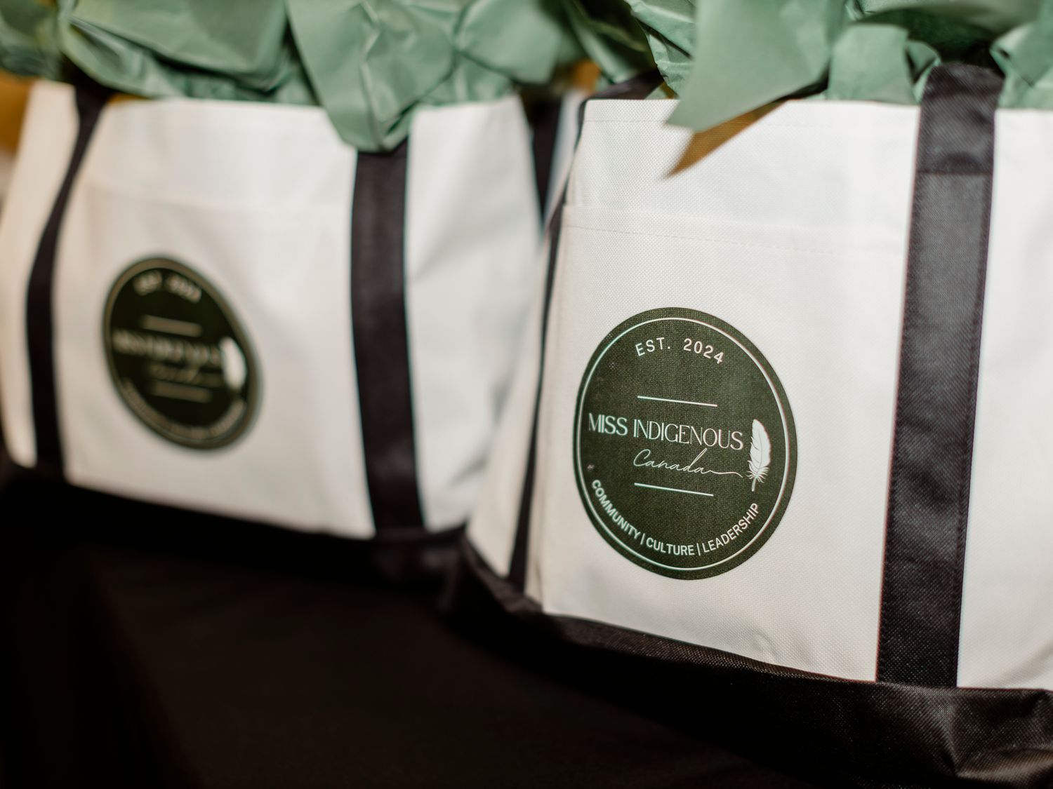 Miss Indigenous Canada EST. 2024 branded tote bags with green tissue paper at an Indigenous pageant event.