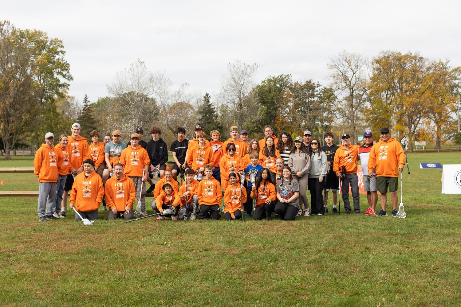 Large group photo of volunteers in orange shirts gathered on grassy field during fall season.