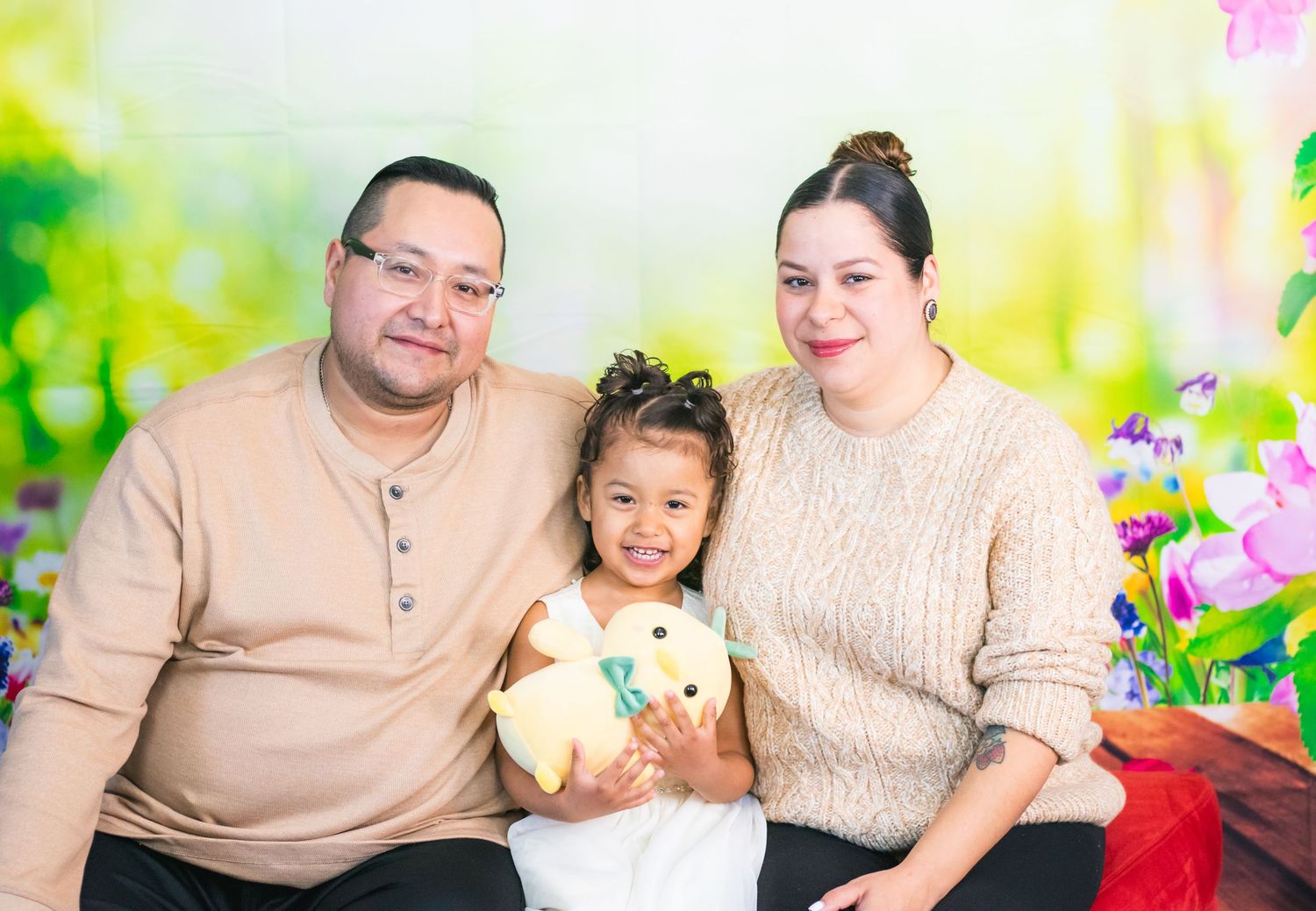 A family photo session with colorful floral backdrop and red velvet seating.