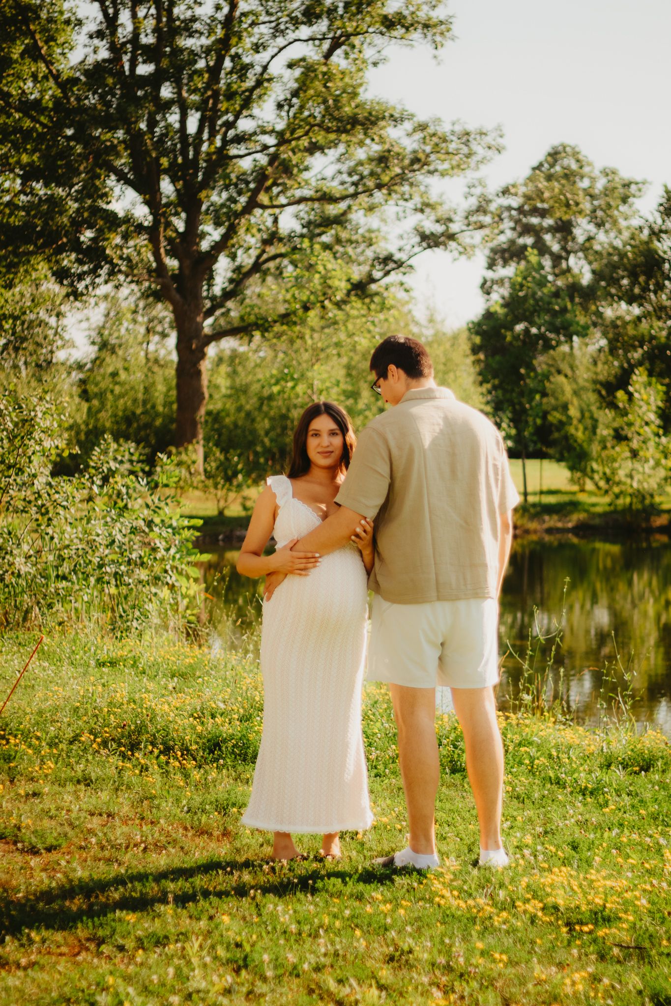 Couple standing by pond during sunset maternity photoshoot.
