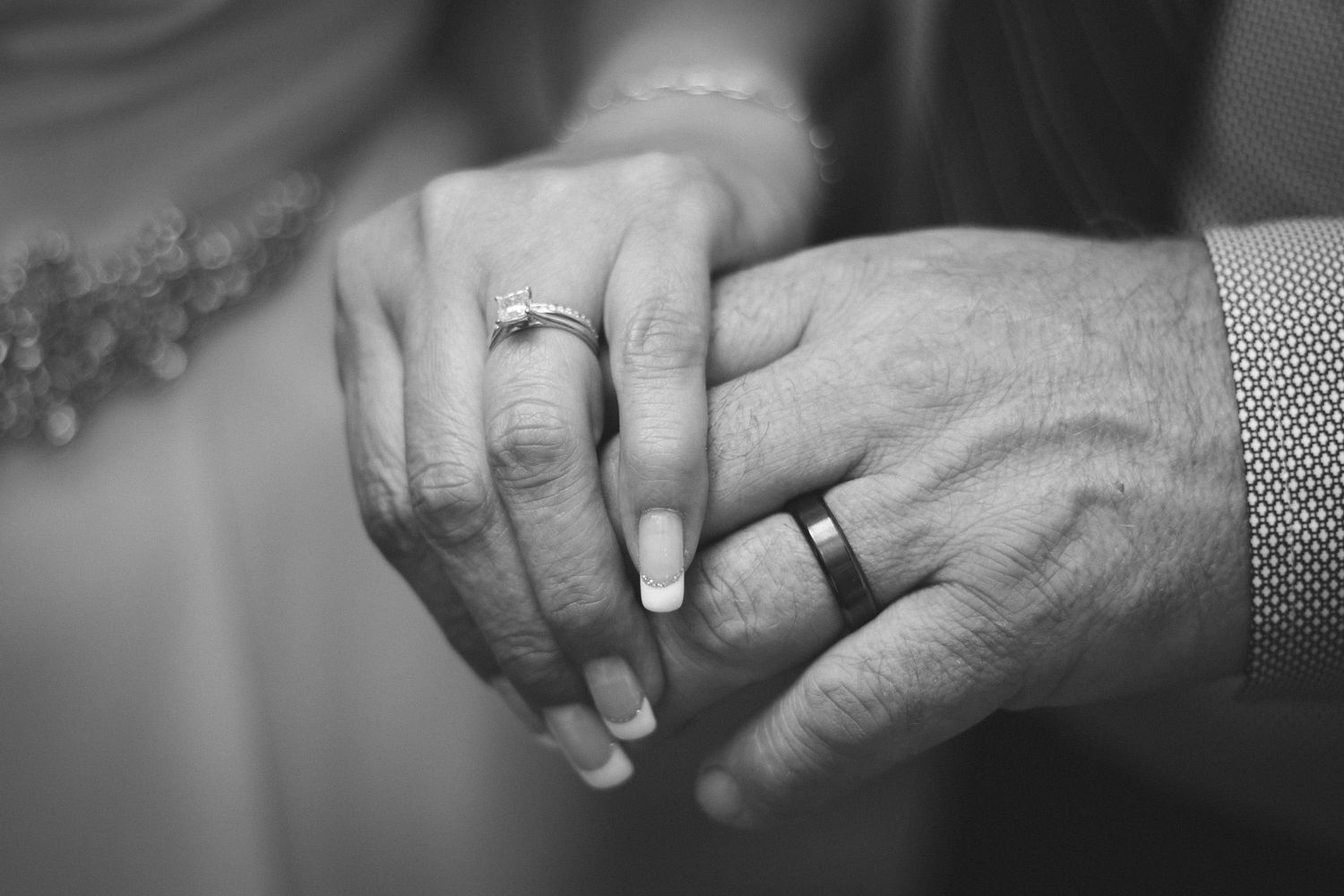 Close-up black and white photo of newlyweds holding hands showing wedding rings.