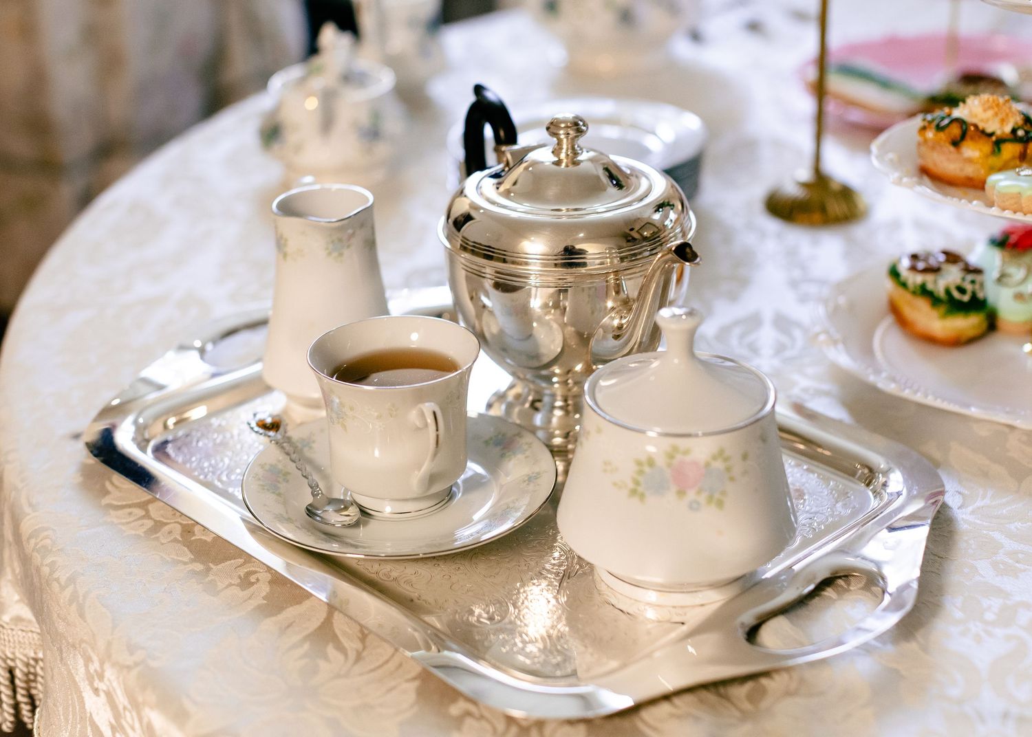 Classic silver tea service set with porcelain cup, creamer, and sugar bowl on ornate tray for elegant tea time.