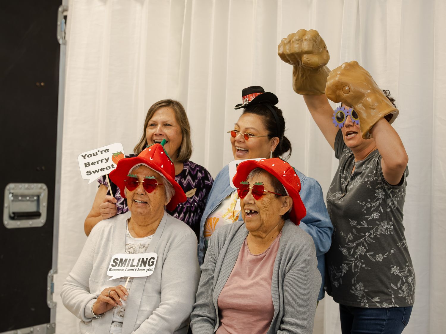 Group of five women posing with fun props in a photo booth at a party.