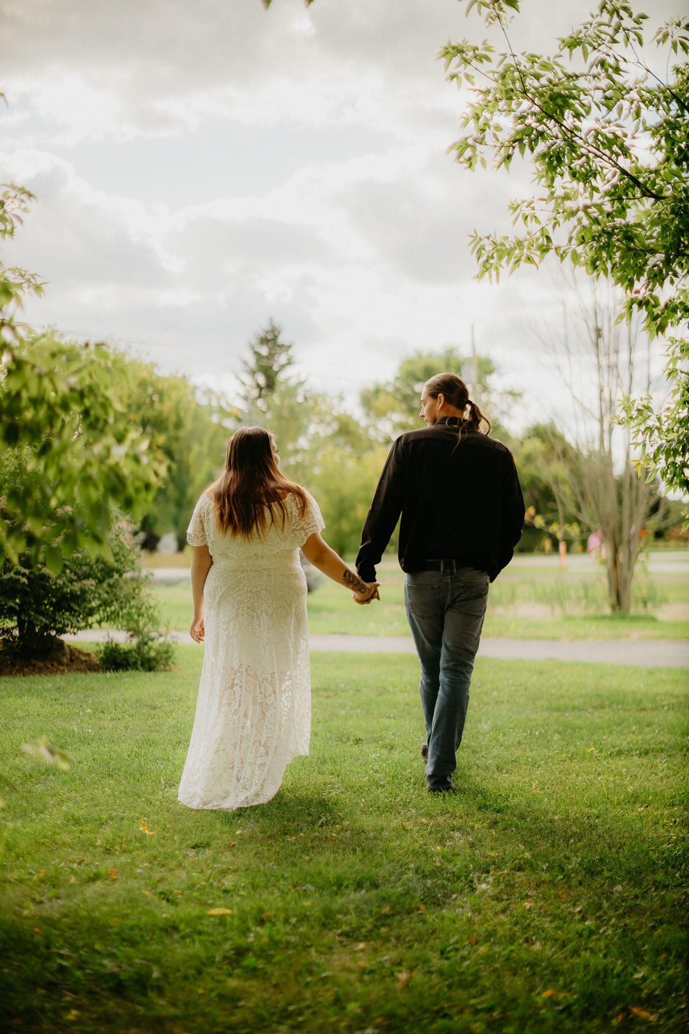 A couple walking hand in hand through a green park on a cloudy day.
