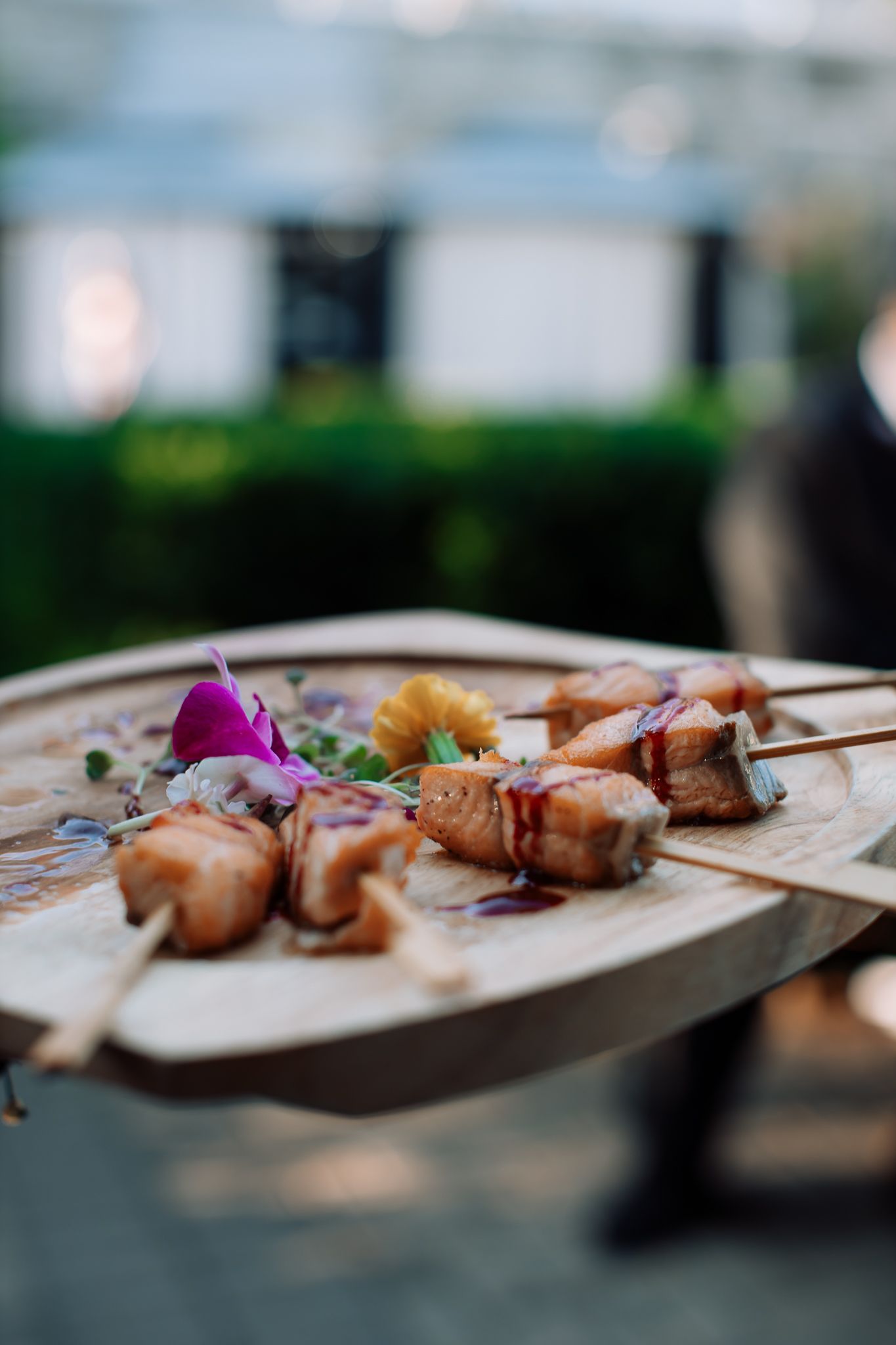 Close-up of grilled skewers garnished with purple flowers on wooden serving boards.