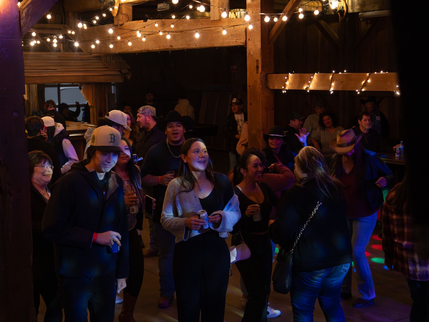 A crowd gathers under warm string lights at an indoor event space.