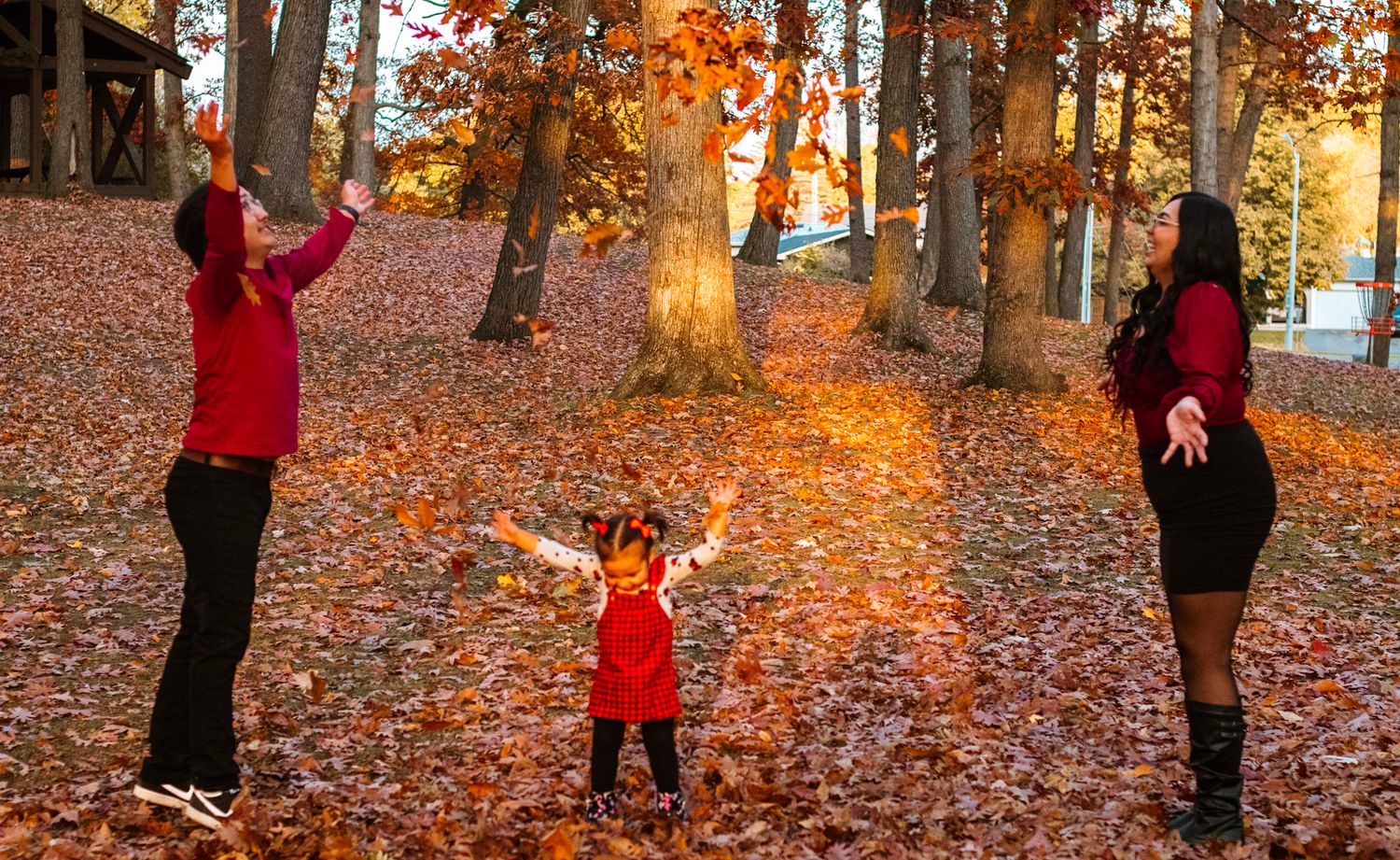 Family playing together in a forest covered with fallen orange autumn leaves.