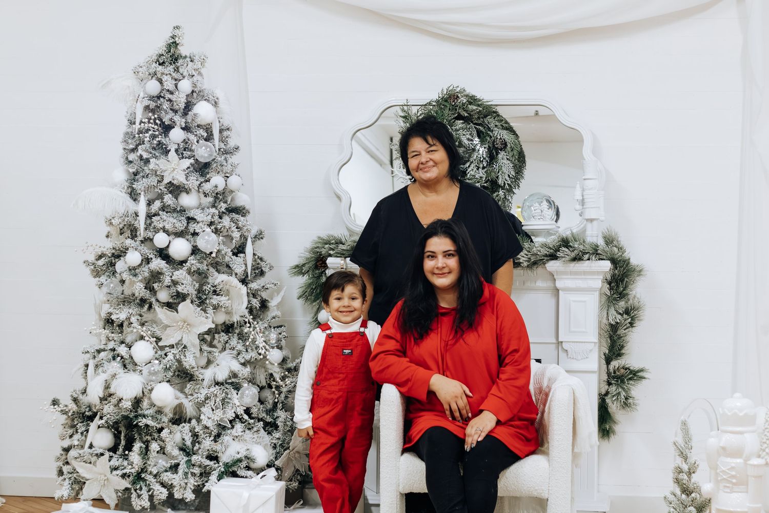 A family group in red and black outfits poses in front of a Christmas fireplace setting.