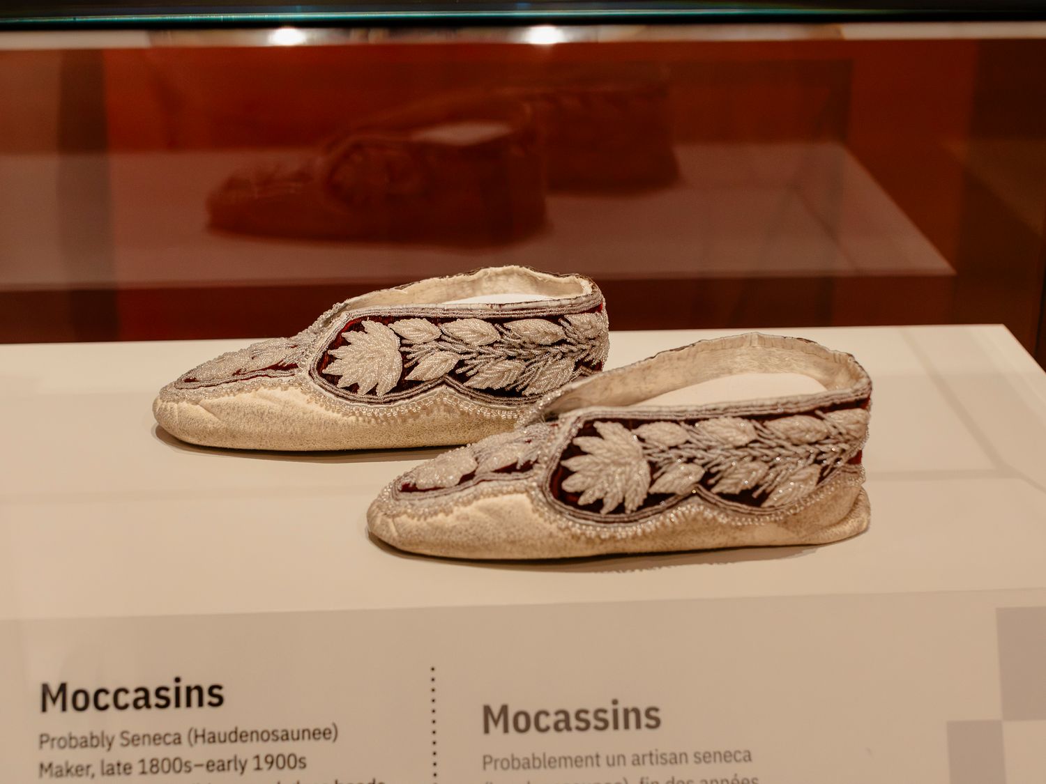 Haudenosaunee Seneca moccasins with intricate floral beadwork on display at a museum, dating from late 1800s to early 1900s.