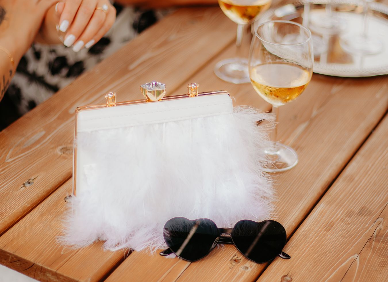 Wine glasses and white feather decorations arranged on rustic wooden table.