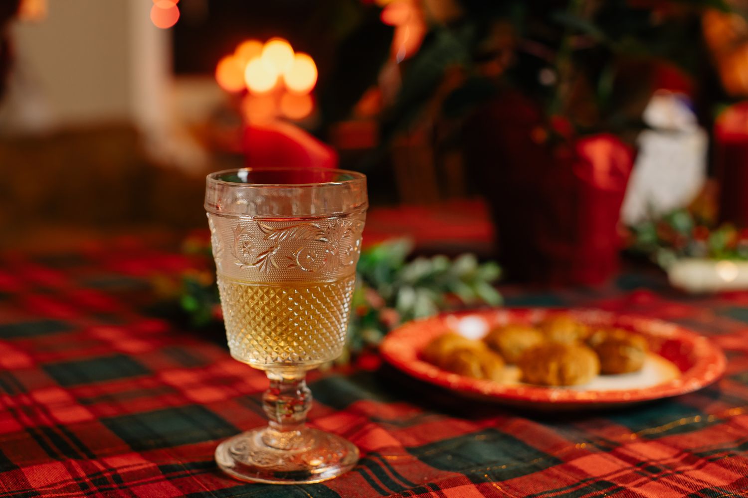 Crystal glasses and holiday decorations on a plaid tablecloth with warm ambient lighting.