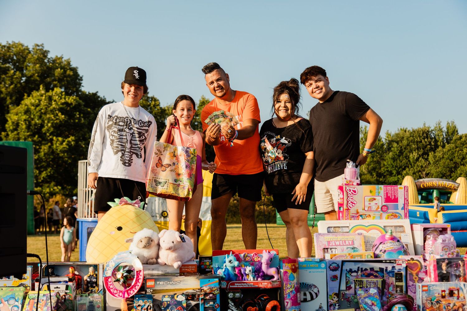 Group poses with collected prizes and toys at an outdoor carnival event.