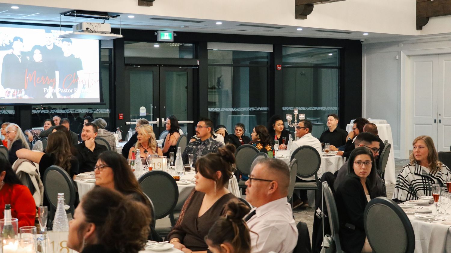 Wide shot of a corporate event space with rows of tables and presentation screens.