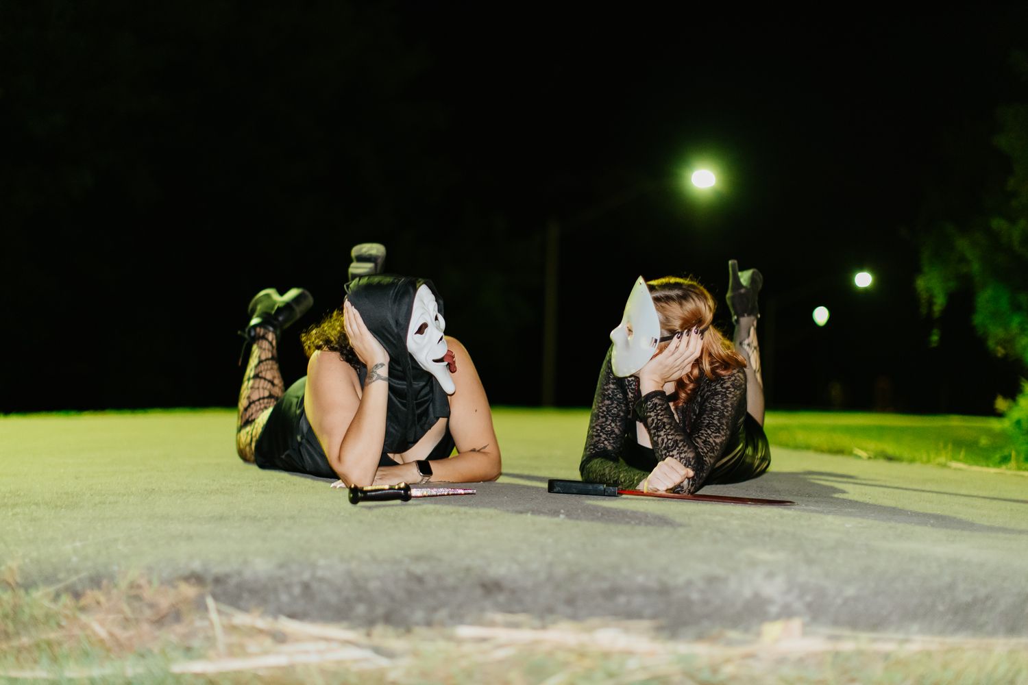 Group in masks resting on pavement at night with green foliage visible in background.