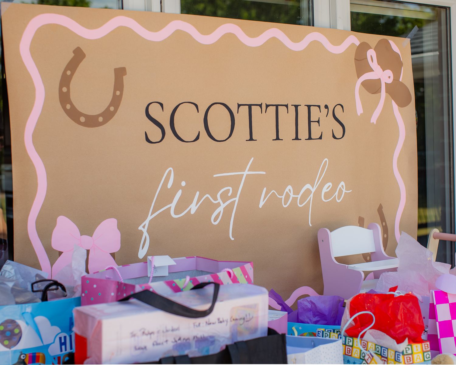 Decorative sign for Scottie's First Rodeo first birthday party surrounded by colorful gift bags.