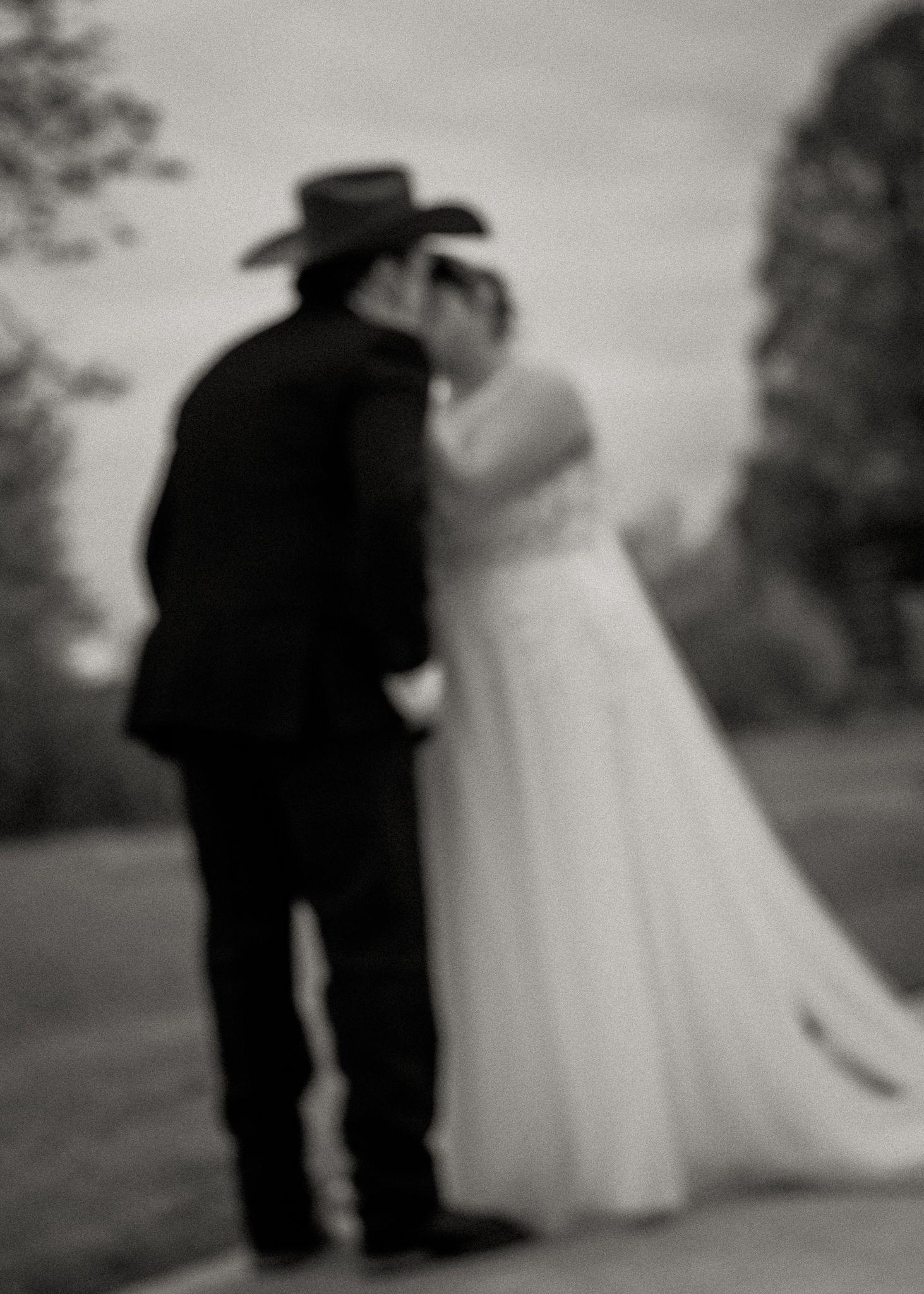 Black and white photo of bride and groom kissing outdoors at sunset wedding.