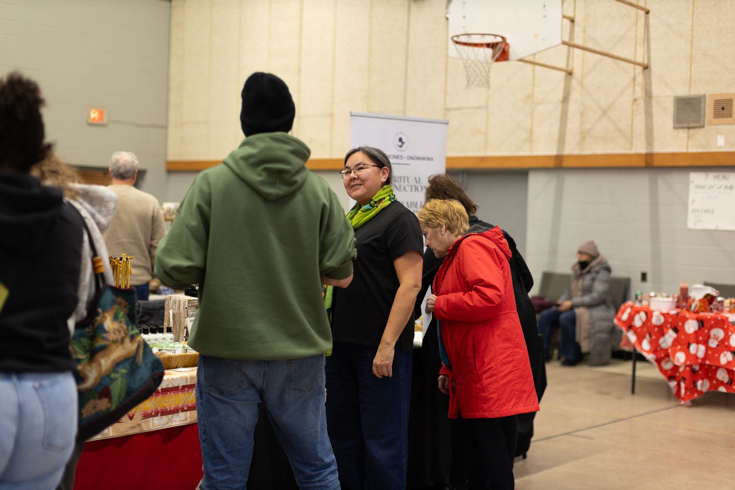 People browsing vendor tables at an indoor holiday market with red decorations.
