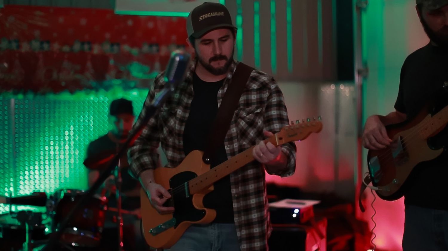 Band members playing instruments under atmospheric red and green stage lighting.