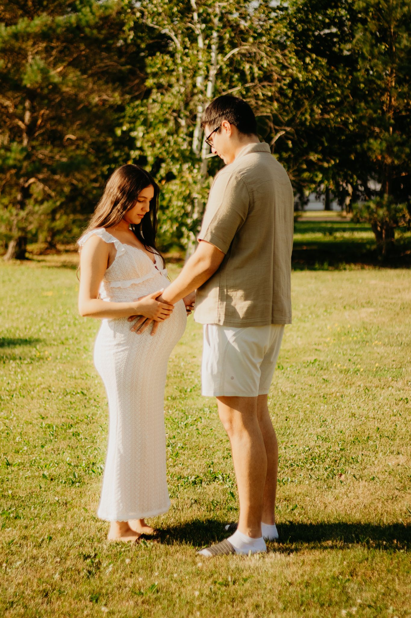 Two people dressed in white share an intimate moment while standing in a park setting.