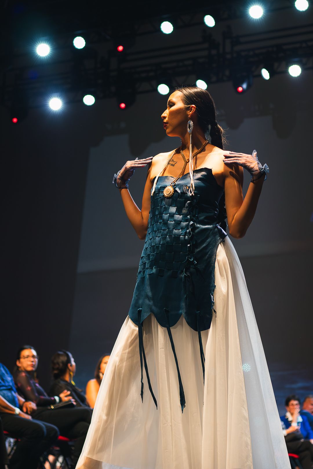 Performer in flowing white and black dress on stage under blue spotlights.