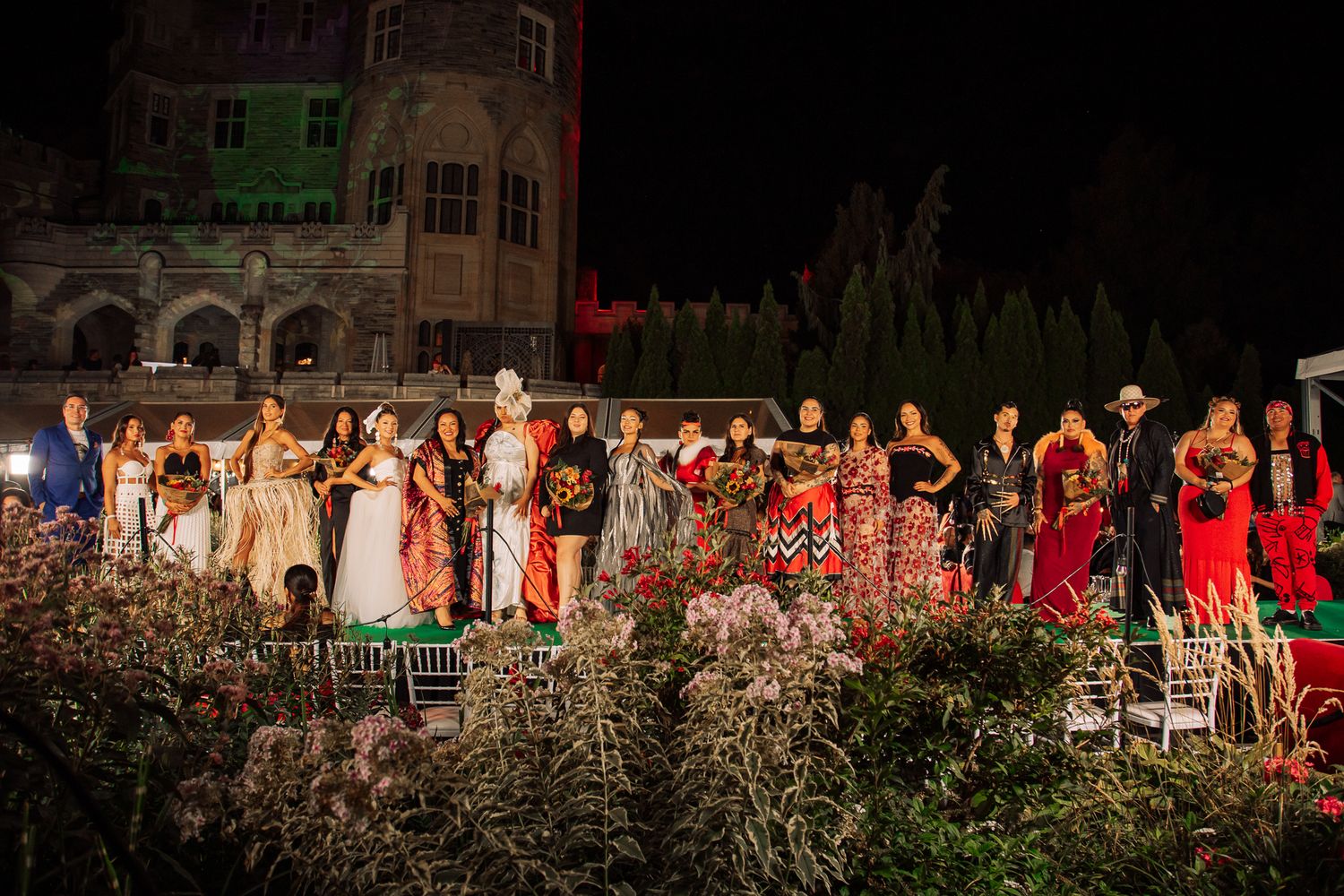 Fashion show audience members seated in rows watching models on a runway at night.