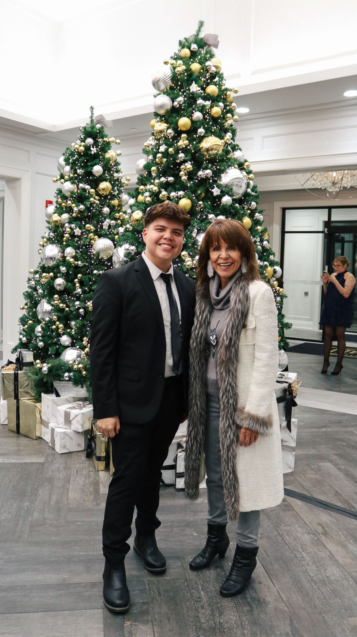 Decorated Christmas trees with gold and white ornaments line a modern indoor space.