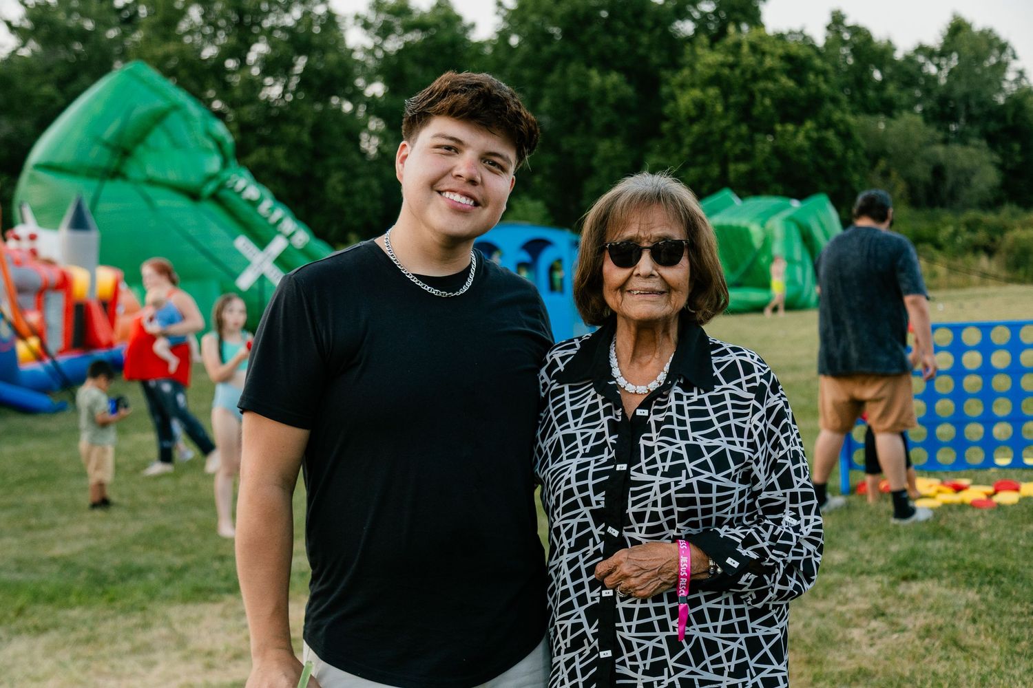 Two people standing together at an outdoor carnival with inflatable attractions in the background.