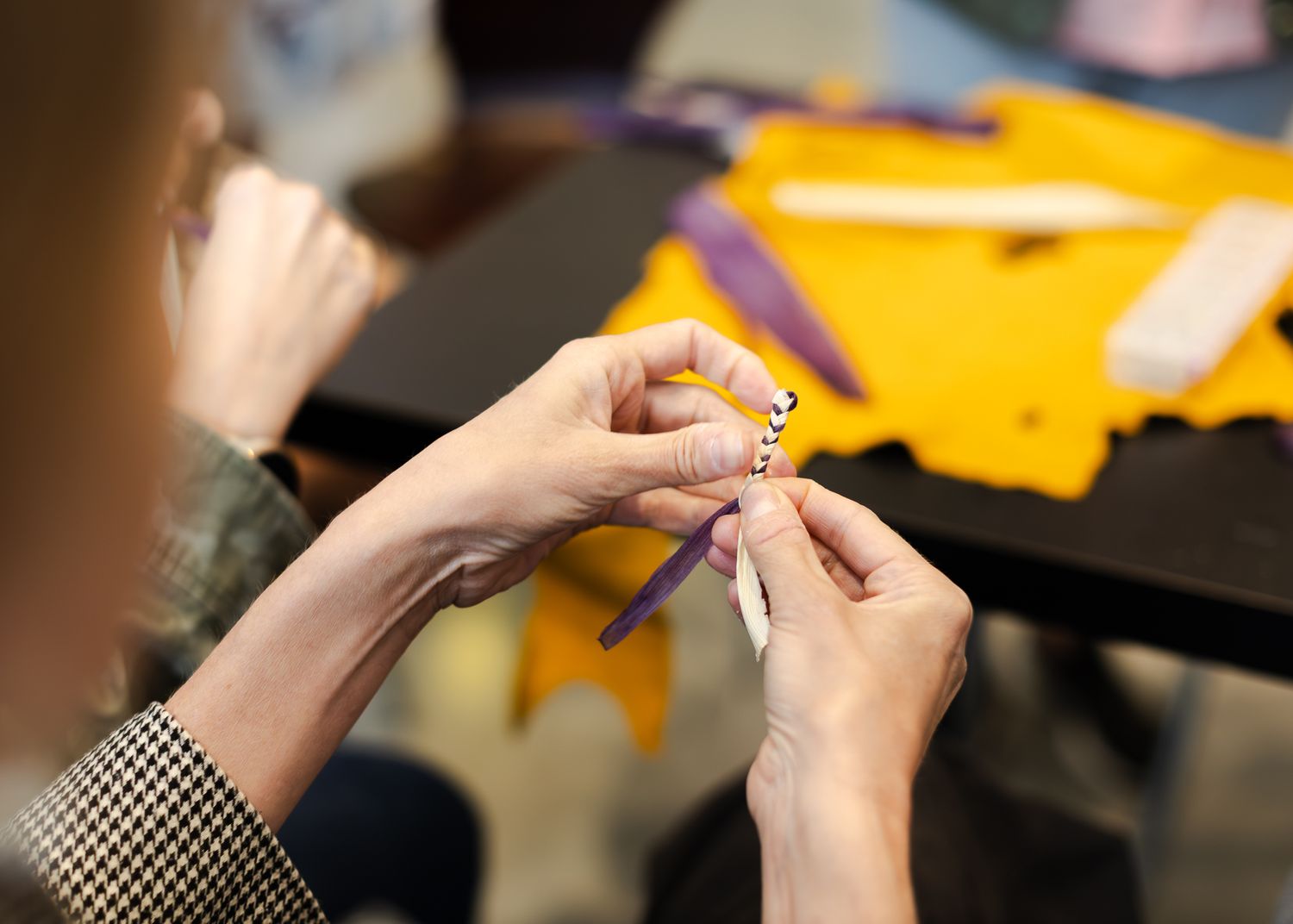 Close-up of hands beading on purple fabric with yellow material and beads on dark table.