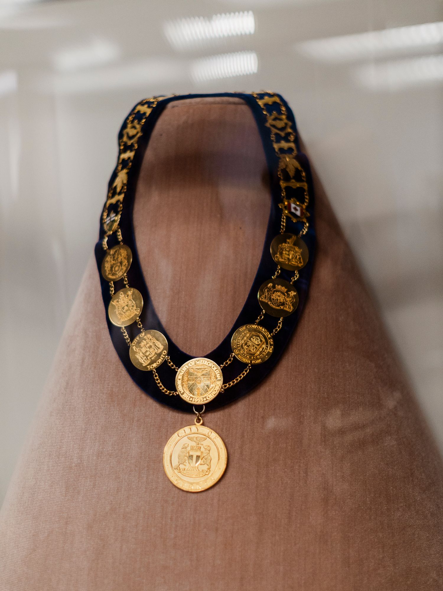 Gold medallion chain necklace with ornate coins on black velvet ribbon displayed on a mannequin bust.