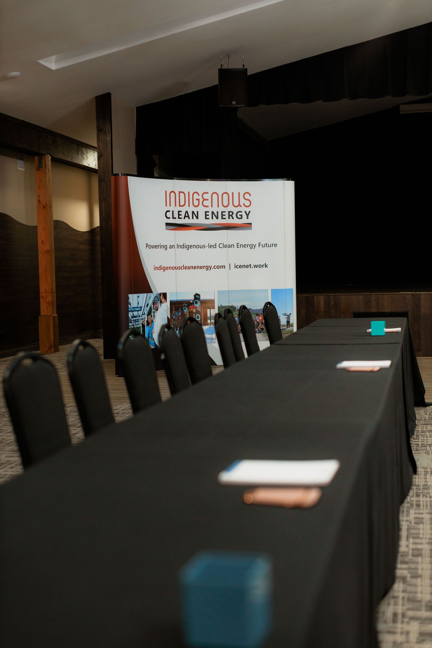 Conference room with long black-draped table and chairs beside an Indigenous Clean Energy organization banner.