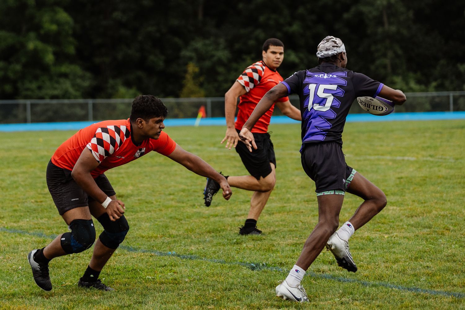 Rugby players in orange and purple jerseys compete during an outdoor flag football game.