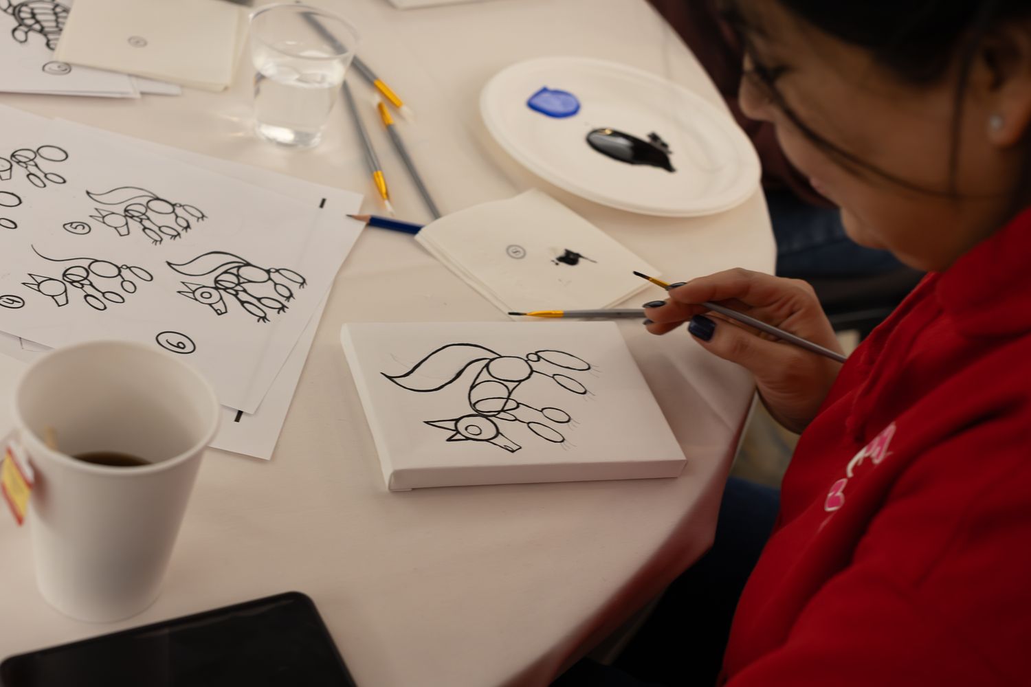 Close-up of people drawing or taking notes at round tables during an event.