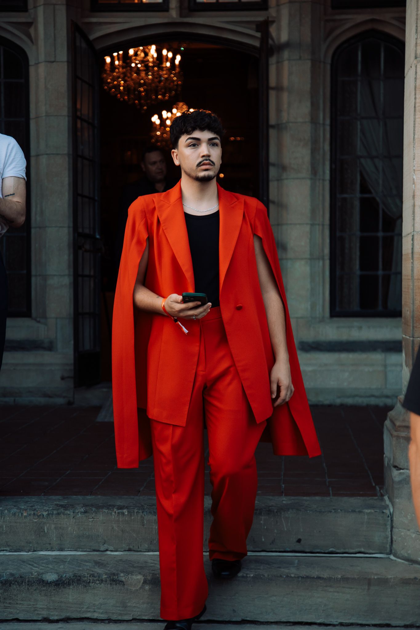 People in red suits and formal attire posing in front of stone building columns.