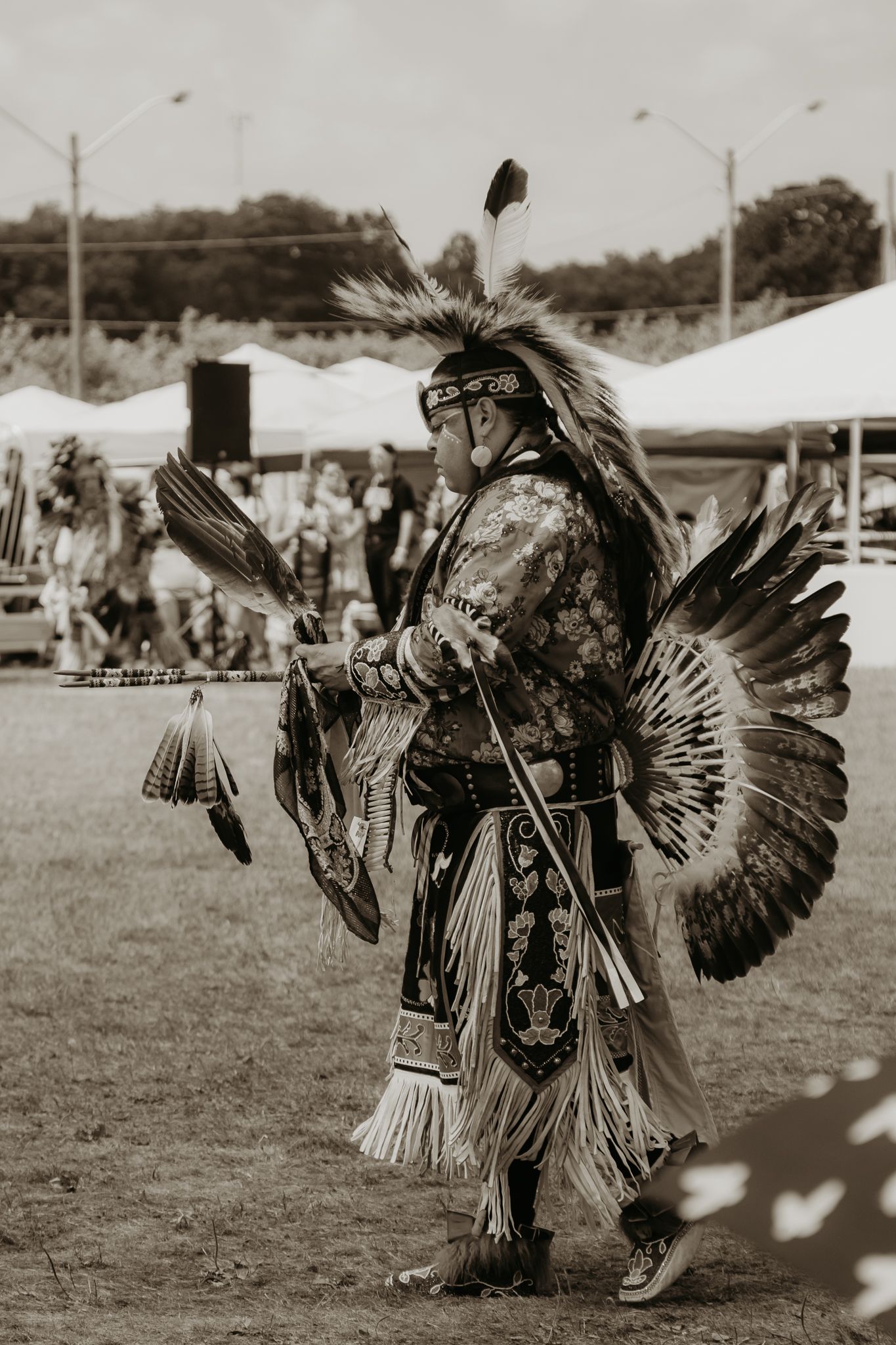 A dancer in traditional Native American regalia with feathered headdress performing at an outdoor event.