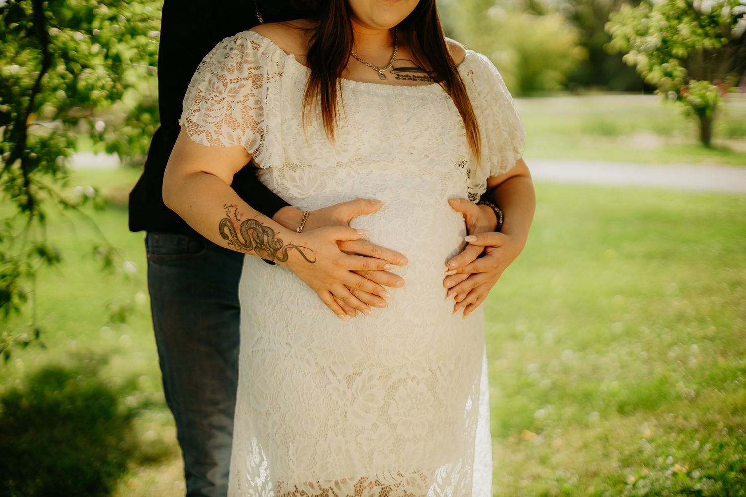 Close up of a lace maternity dress with hands resting on a pregnant belly.
