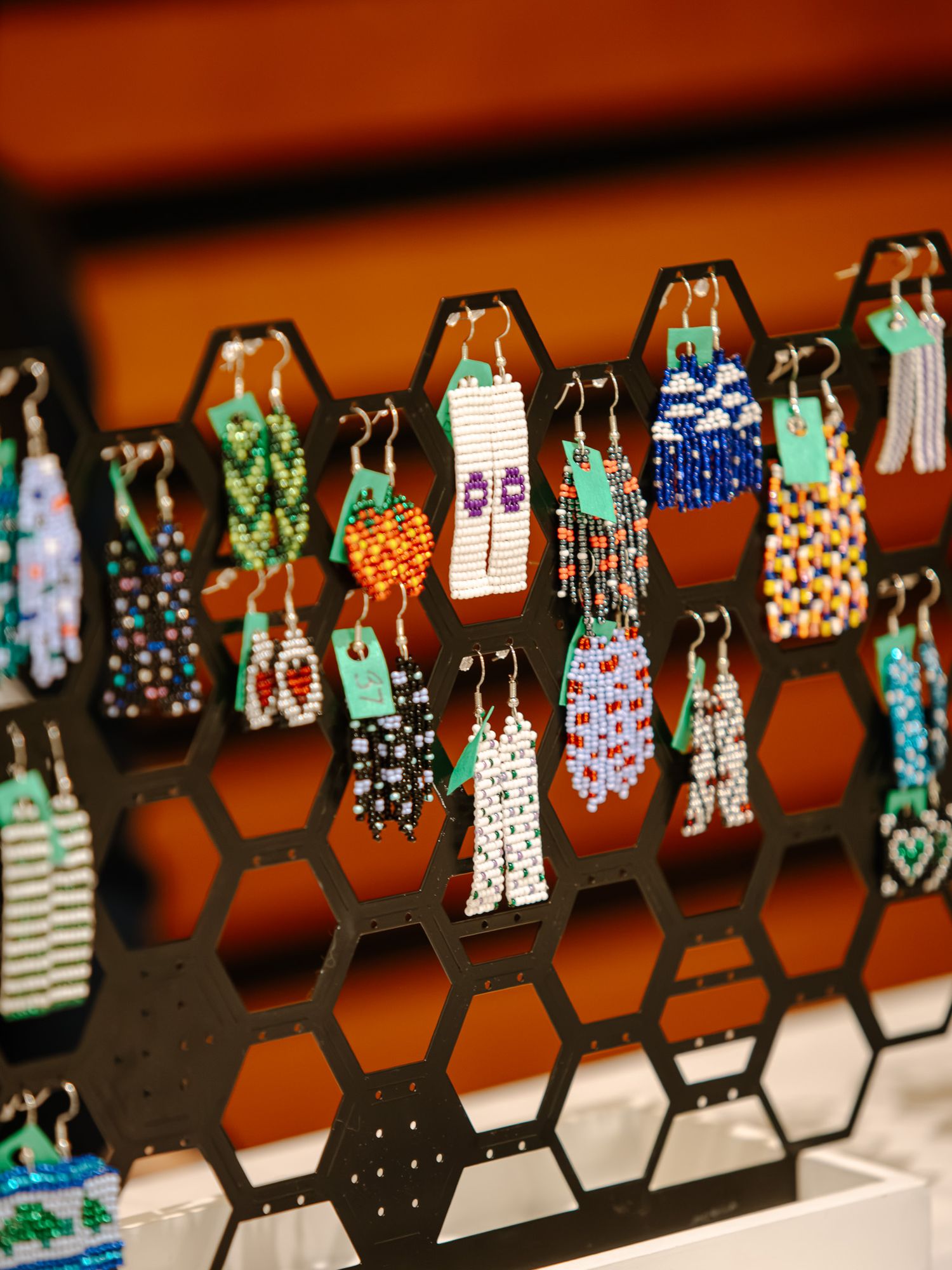 Colorful beaded earrings displayed on a black honeycomb earring stand at a jewelry market or craft fair.