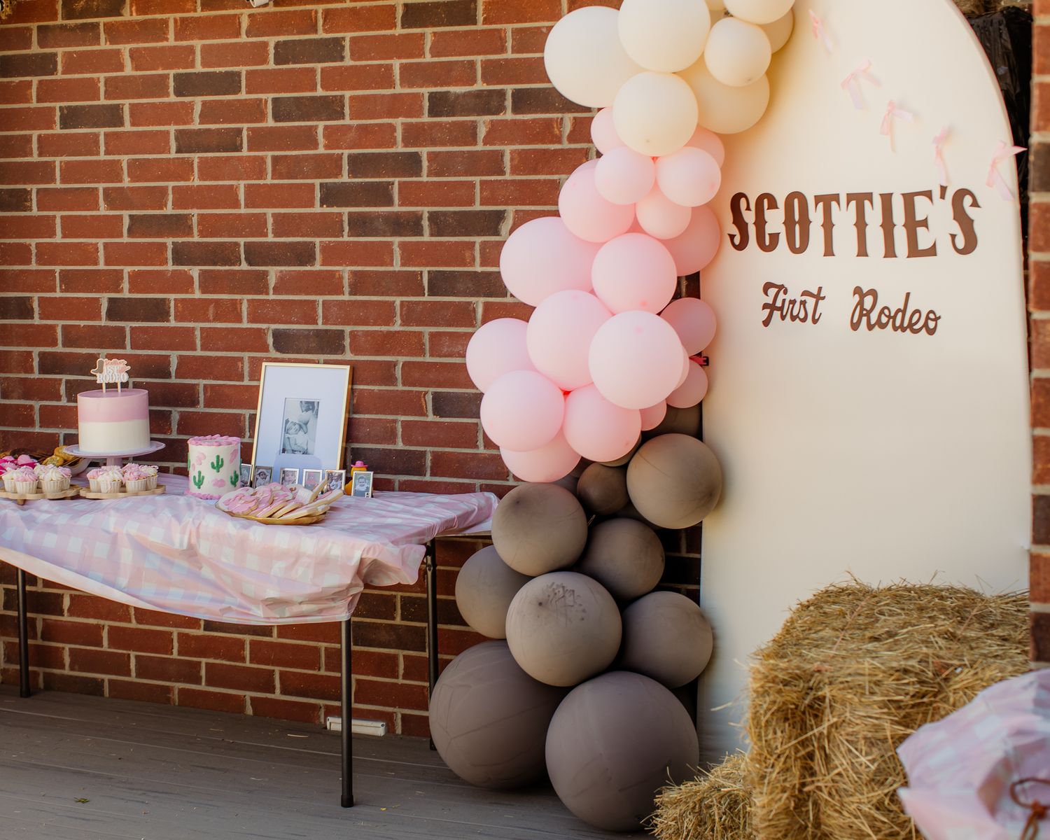 Pink and brown balloon arch beside a wooden sign reading Scottie's First Rodeo at a cowgirl birthday party.