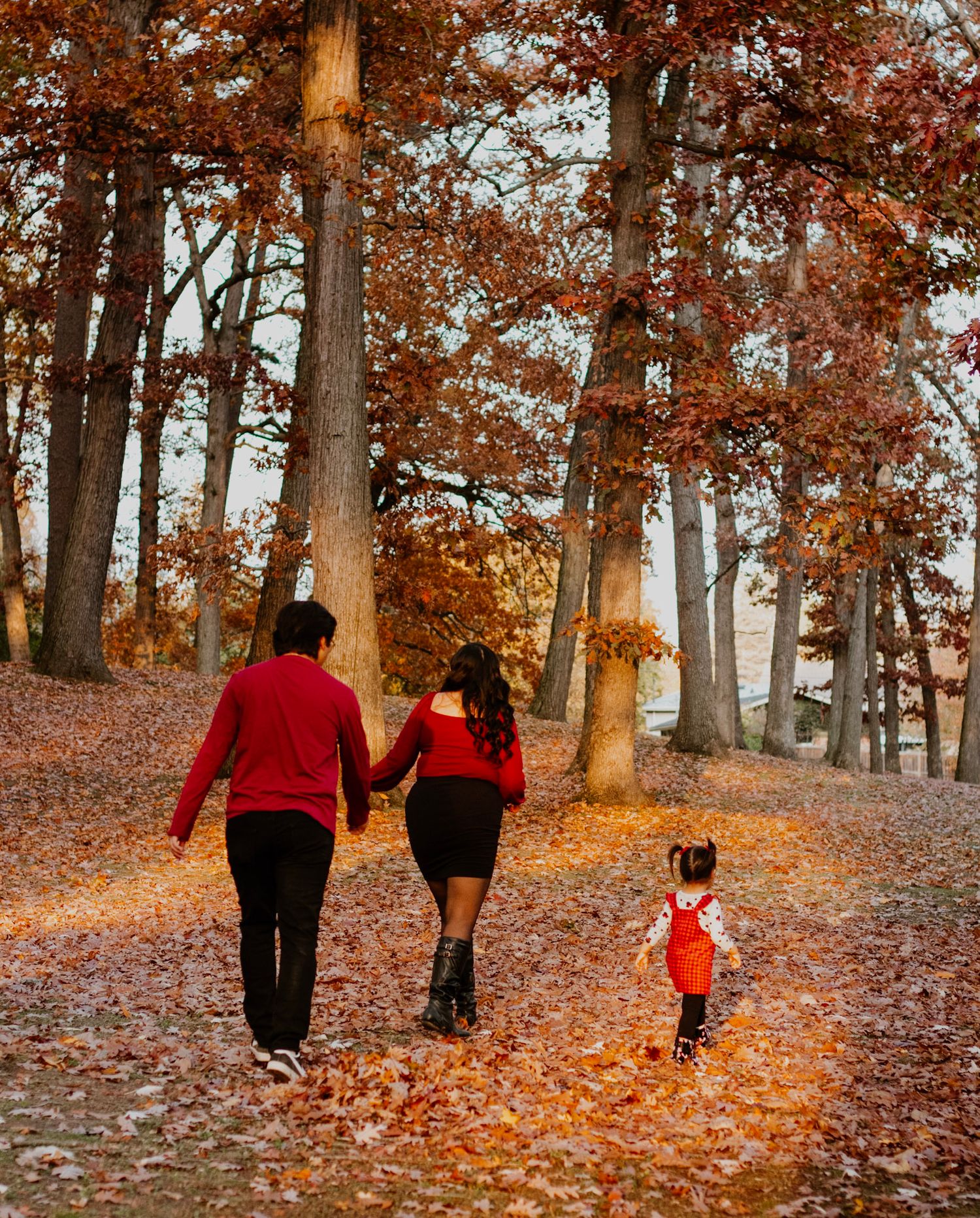 Family walking hand in hand through autumn forest with fallen leaves.