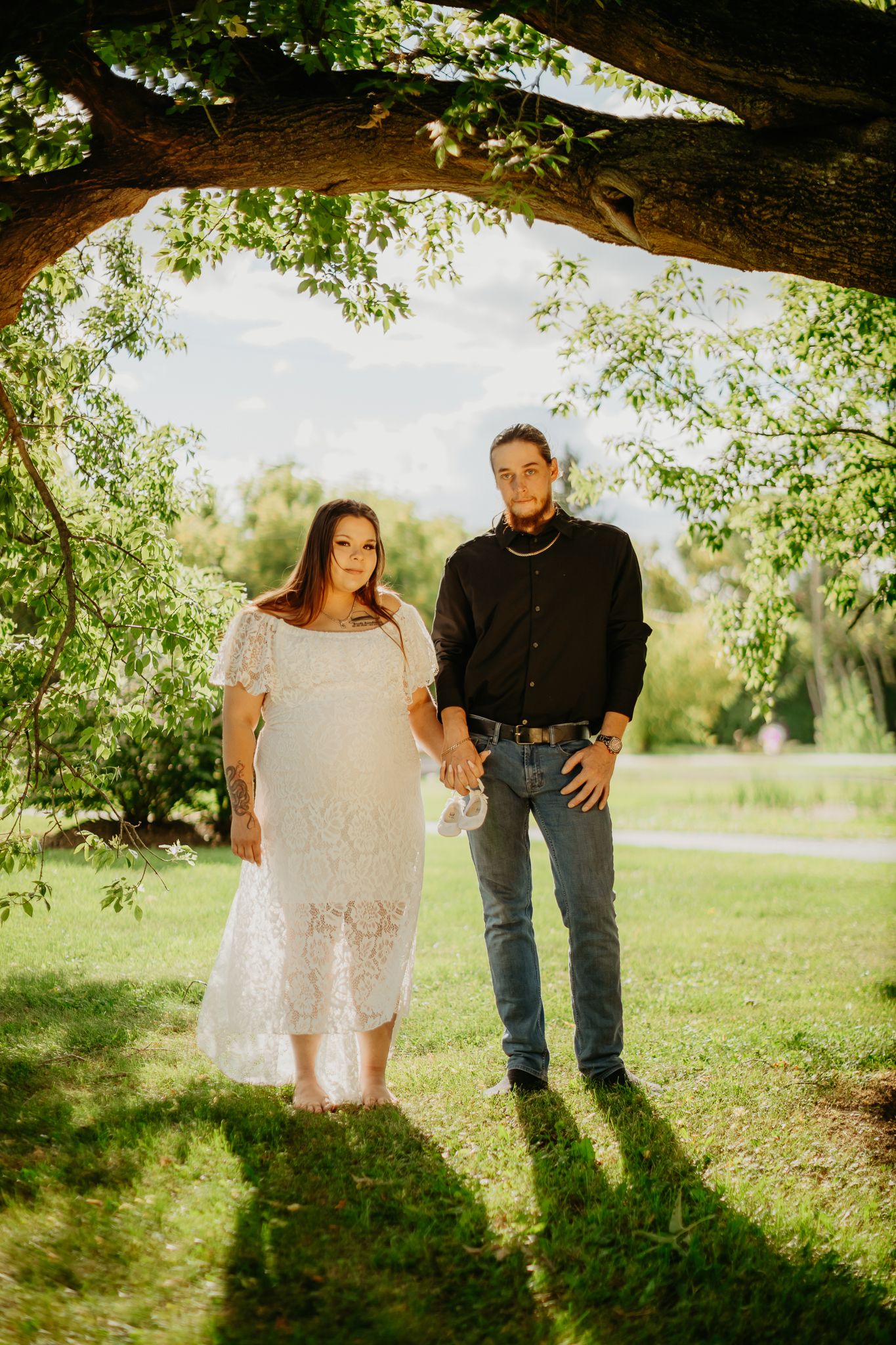 A couple stands under a large tree branch in golden afternoon sunlight.