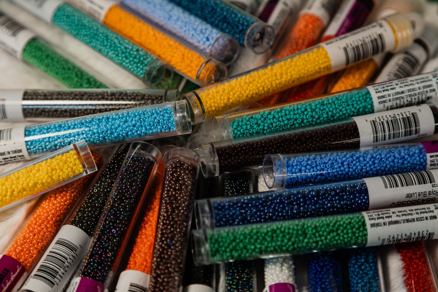 Colorful seed beads in clear labeled tubes, organized in a pile, perfect for jewelry making and crafting projects.